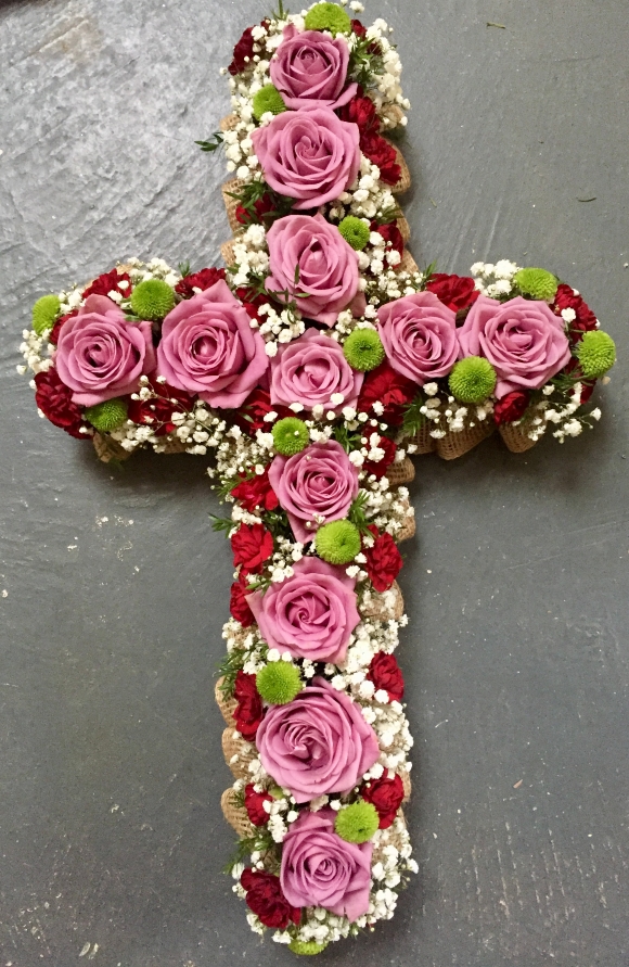 A cross having mauve, red, green and white on a hessian base